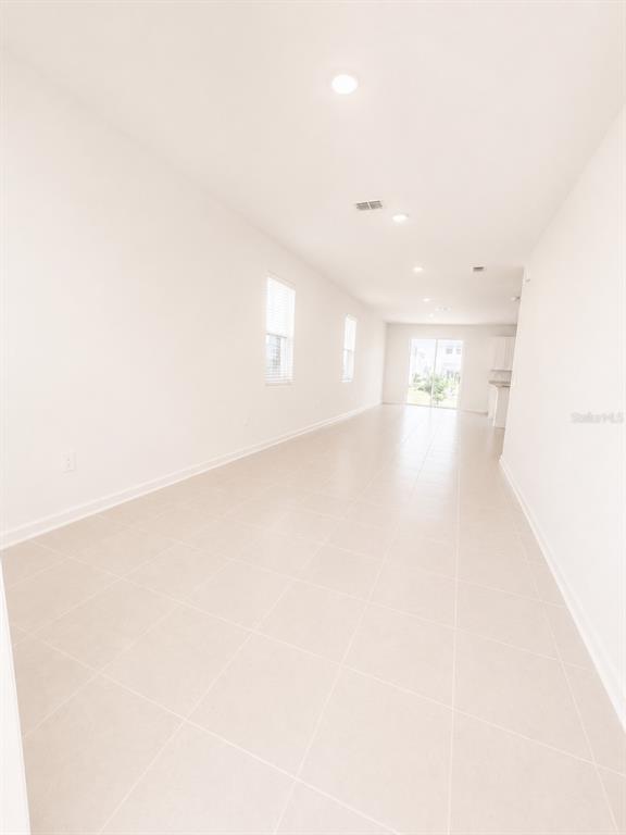 An empty, long room features white walls, recessed lighting, and light-colored tile flooring — 3115 MINDFULLNESS DRIVE, CLERMONT, FL