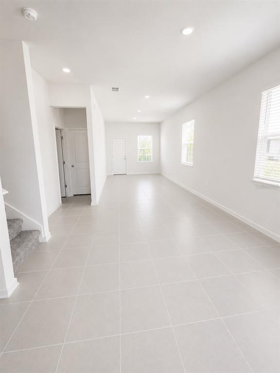 An empty room with light-colored tile flooring, white walls, recessed lighting, and a staircase — 3115 MINDFULLNESS DRIVE, CLERMONT, FL
