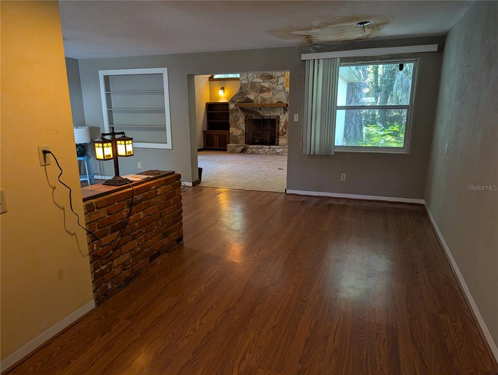 A living room with wood-look flooring, a brick half-wall, and a stone fireplace beyond — 308 TRUDGEON DRIVE, NEW SMYRNA BEACH, FL