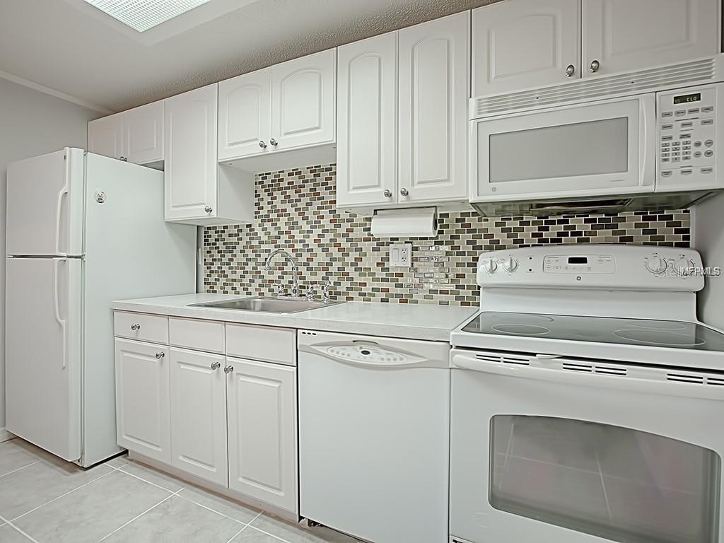 A kitchen features white cabinetry, white appliances, a mosaic tile backsplash, and light-colored countertops — 4073 E MICHIGAN STREET UNIT 4073, ORLANDO, FL