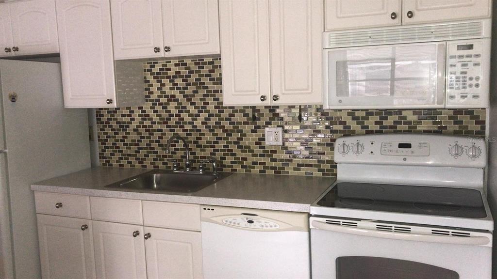 A kitchen features white cabinets, a mosaic tile backsplash, a stainless sink, and white appliances — 4073 E MICHIGAN STREET UNIT 4073, ORLANDO, FL