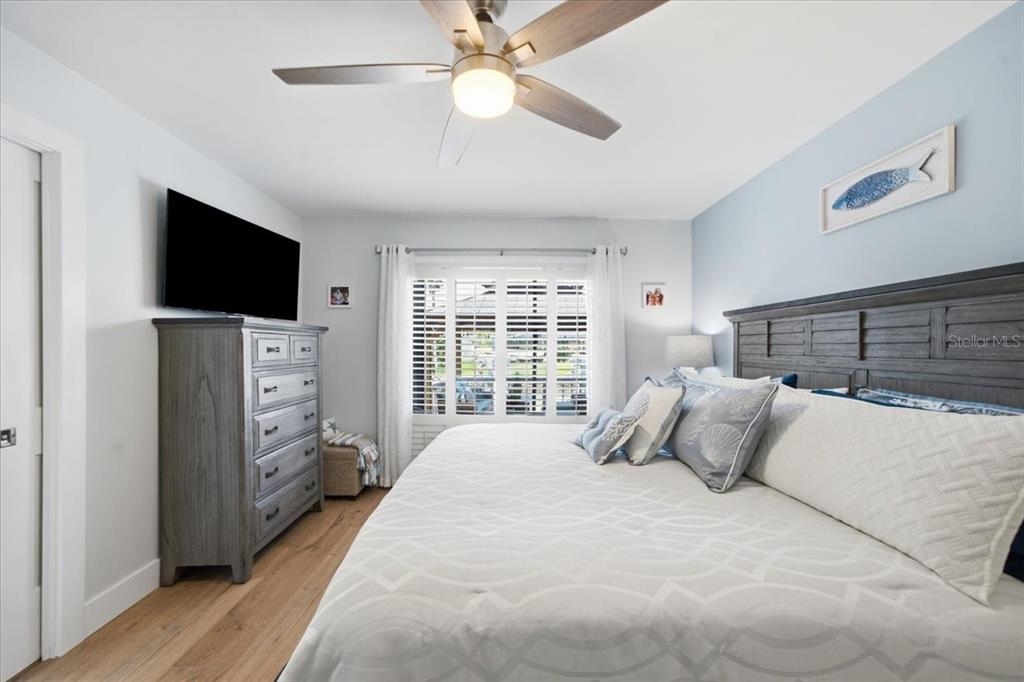 A bedroom features a king bed, a gray dresser with a television, and plantation shutters — 5214 S RIVERVIEW CIRCLE, HOMOSASSA, FL
