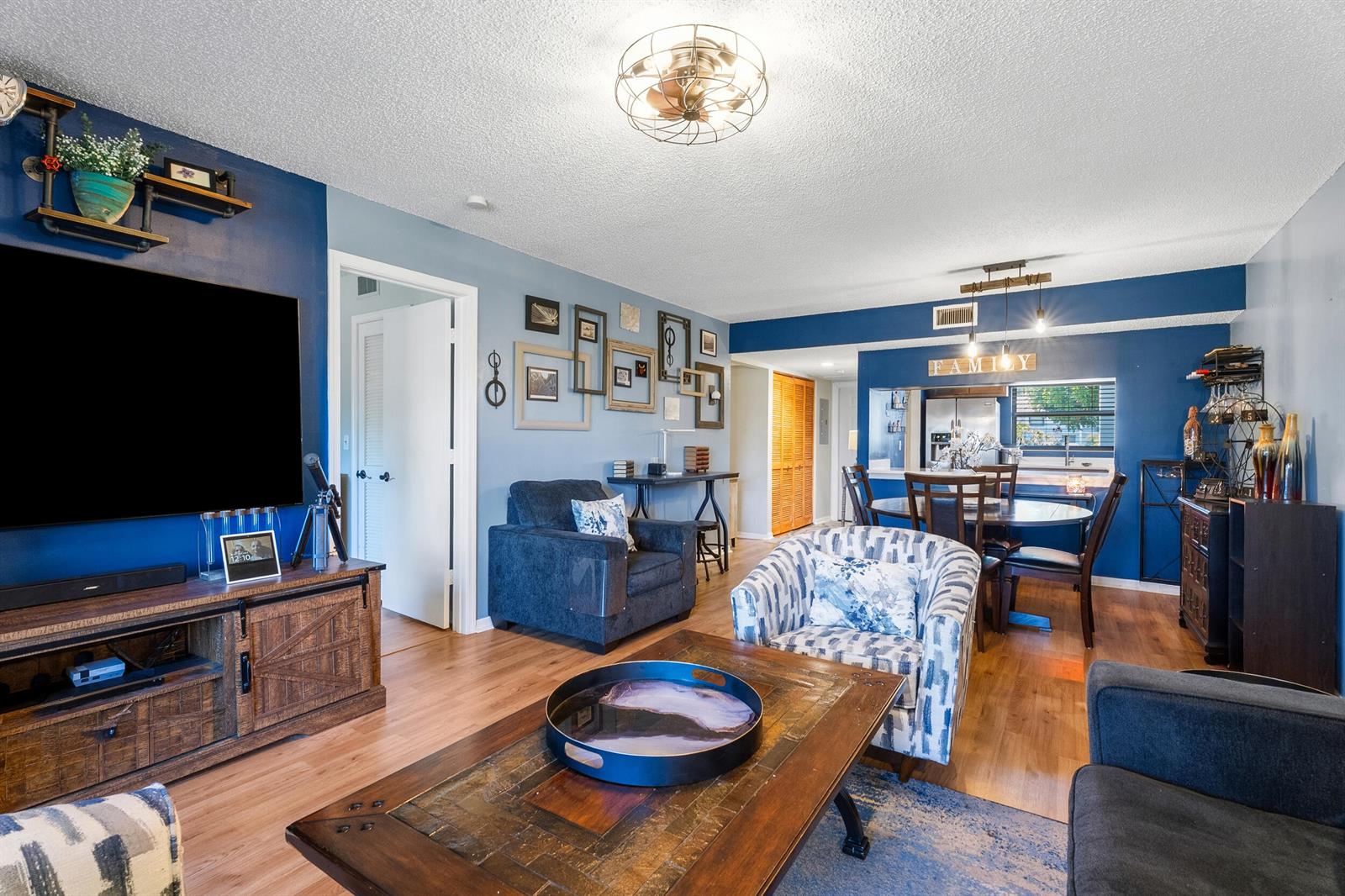 A living room with blue walls, a wood media console, and an adjacent dining area — 1201 SE Parkview Place # G4, Stuart FL 34994, STUART, FL