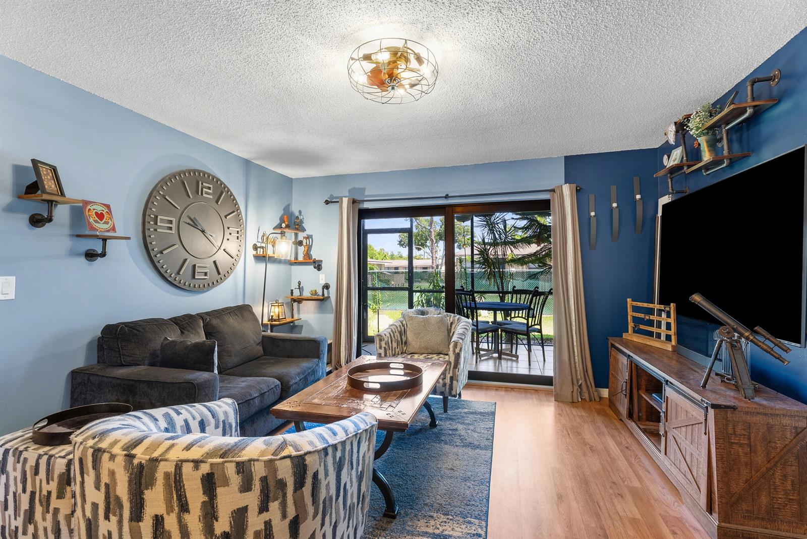 A living room features blue walls, a large wall clock, patterned armchairs, and a sliding door — 1201 SE Parkview Place # G4, Stuart FL 34994, STUART, FL