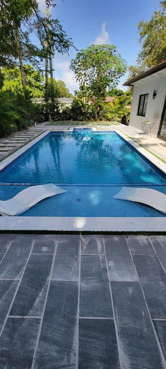 A rectangular swimming pool with two submerged lounge chairs sits in a paved backyard — 5901 SW 64th St, South Miami FL 33143, SOUTH MIAMI, FL