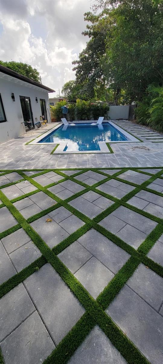 A backyard features a rectangular swimming pool surrounded by gray pavers and artificial turf strips — 5901 SW 64th St, South Miami FL 33143, SOUTH MIAMI, FL