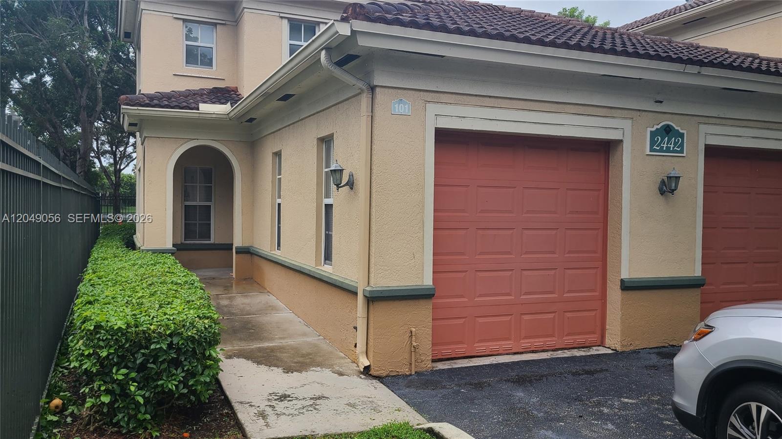 A two-story tan stucco building features a red garage door and a concrete walkway — 2442 Centergate Dr # 101, Miramar FL 33025, MIRAMAR, FL