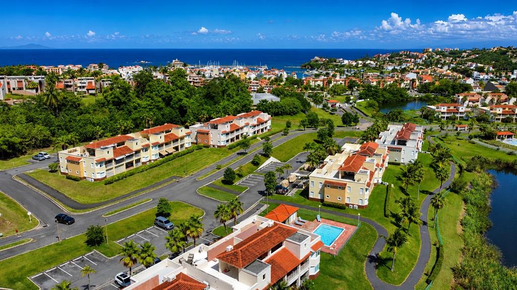 An aerial view shows multi-story apartment buildings with red-tiled roofs near a coastal town — Palmas Drive COND. HARBOUR LAKES UNIT 26, HUMACAO, PR