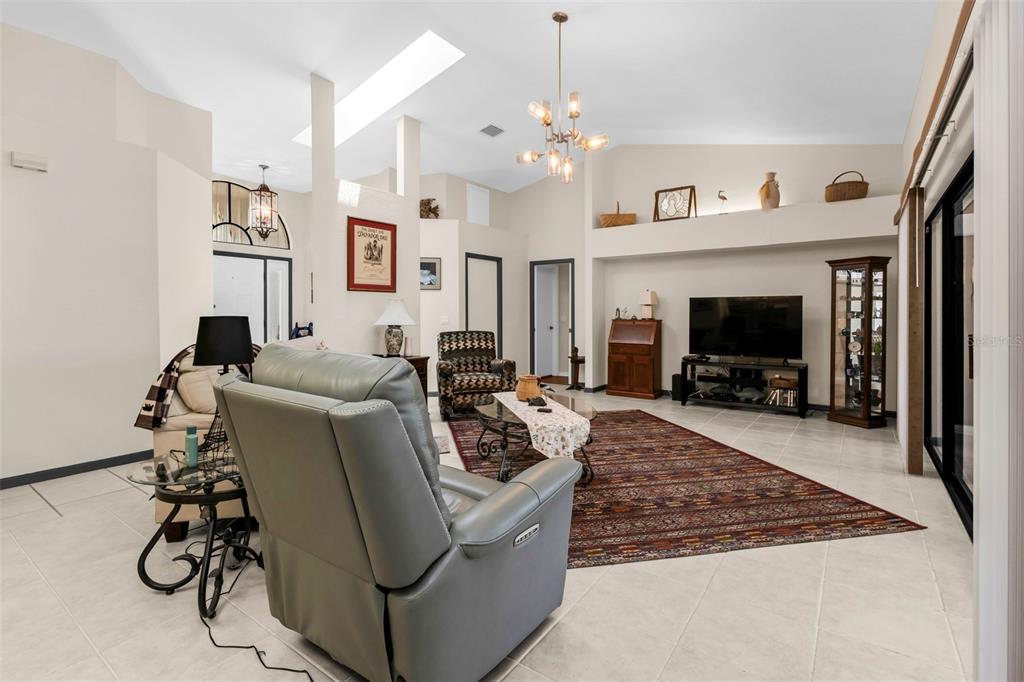 A living room features a vaulted ceiling, tile flooring, a large area rug, and a television — 239 VALDIVA STREET, PUNTA GORDA, FL