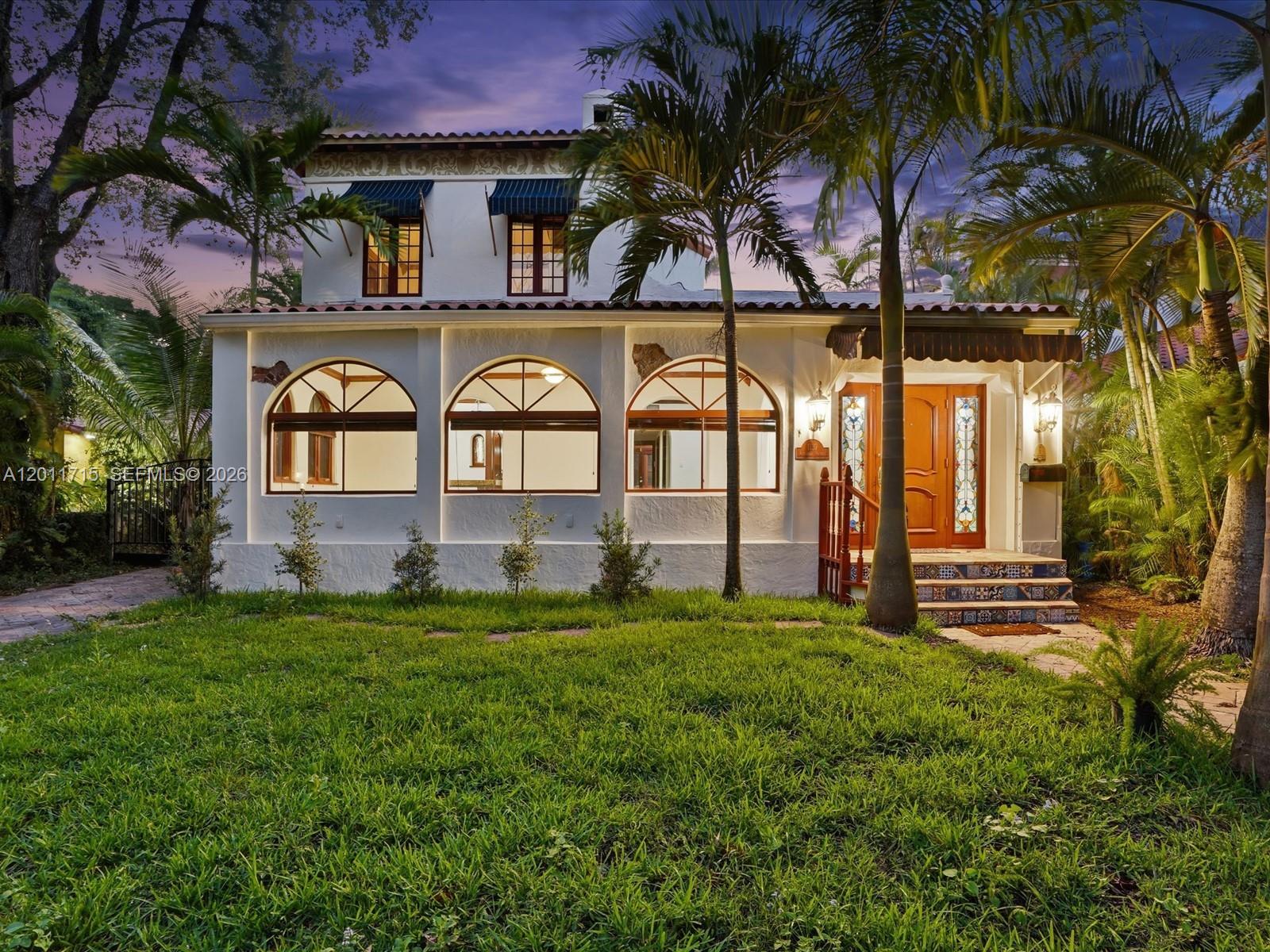 A two-story white stucco house with arched windows and a tiled entryway at dusk — 1137 Asturia Ave, Coral Gables FL 33134, CORAL GABLES, FL