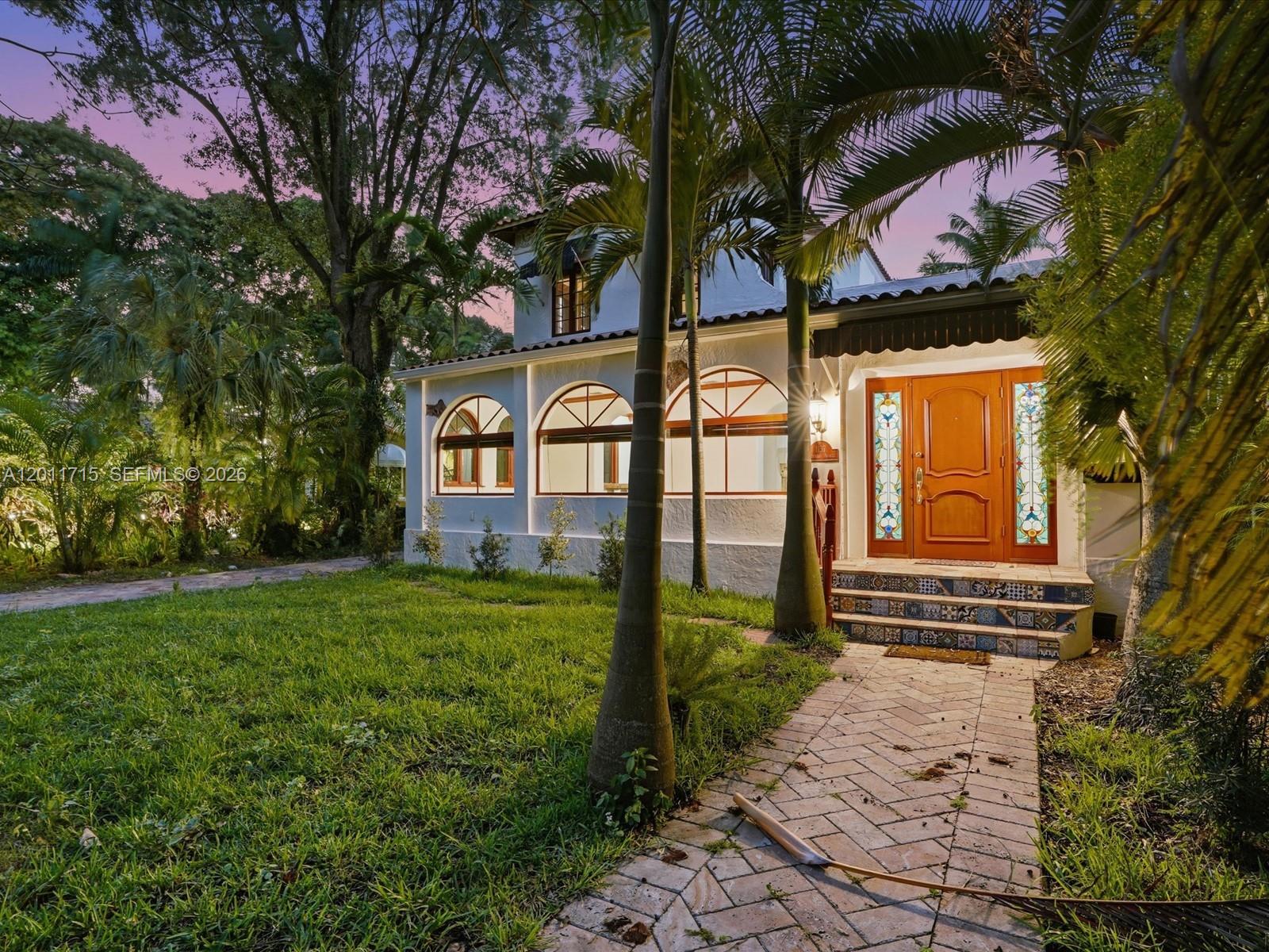 A white two-story house features arched windows, a stained-glass front door, and tiled steps — 1137 Asturia Ave, Coral Gables FL 33134, CORAL GABLES, FL