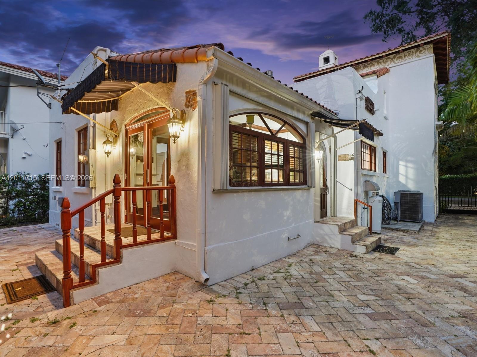 The exterior of a white stucco building features a brick patio, arched windows, and awnings — 1137 Asturia Ave, Coral Gables FL 33134, CORAL GABLES, FL