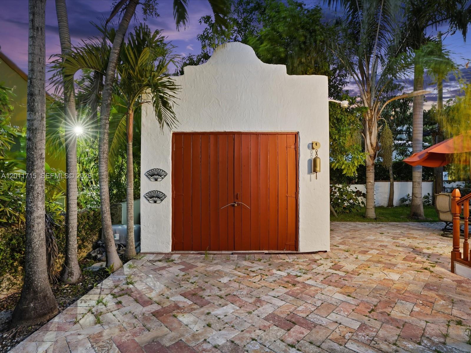 A white stucco building with a mission-style roof and double wooden doors sits outdoors — 1137 Asturia Ave, Coral Gables FL 33134, CORAL GABLES, FL