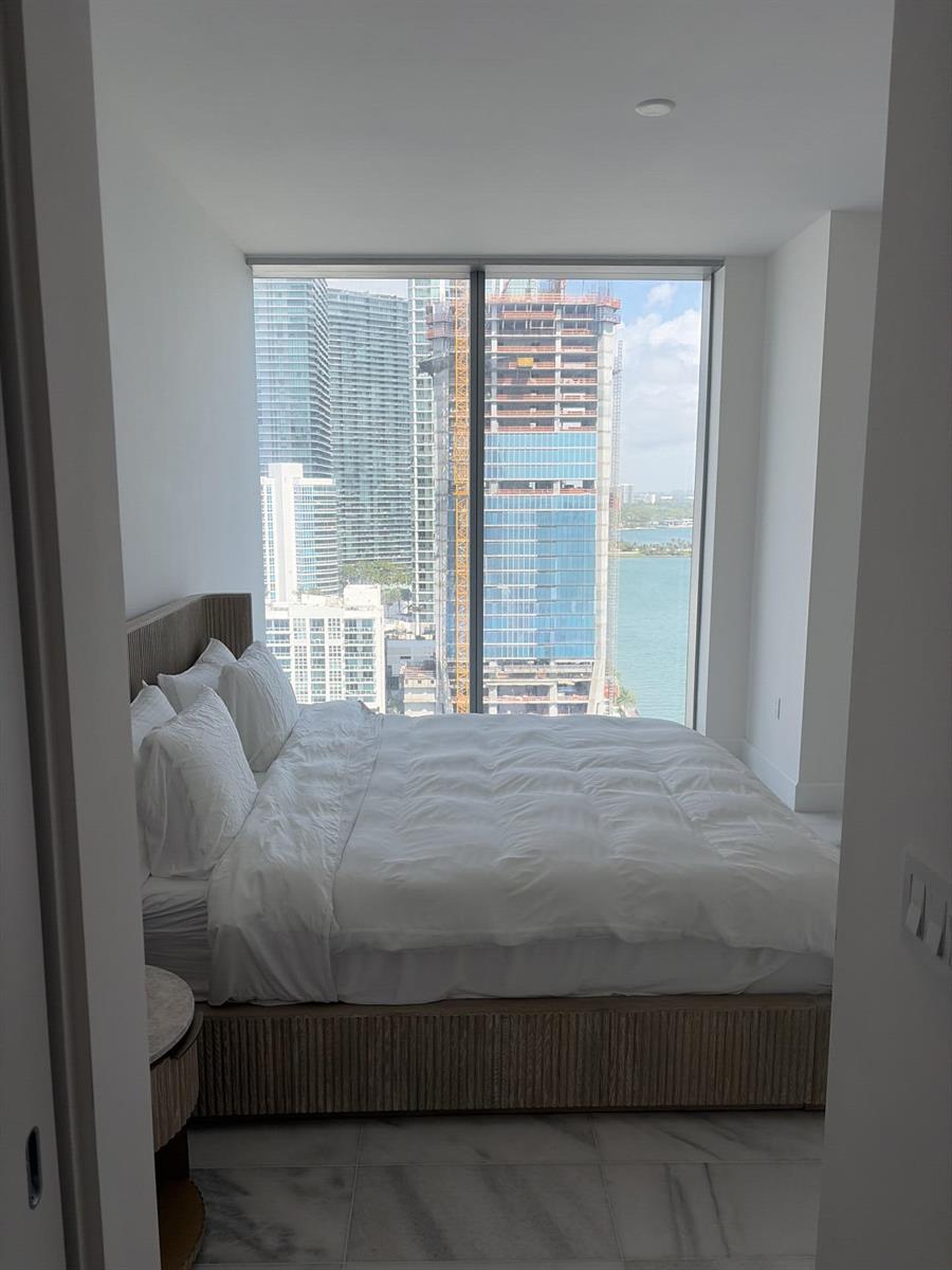A bedroom with a platform bed faces floor-to-ceiling windows overlooking a city skyline and water — 700 NE 26th Terrace # 2006, Miami FL 33137, MIAMI, FL