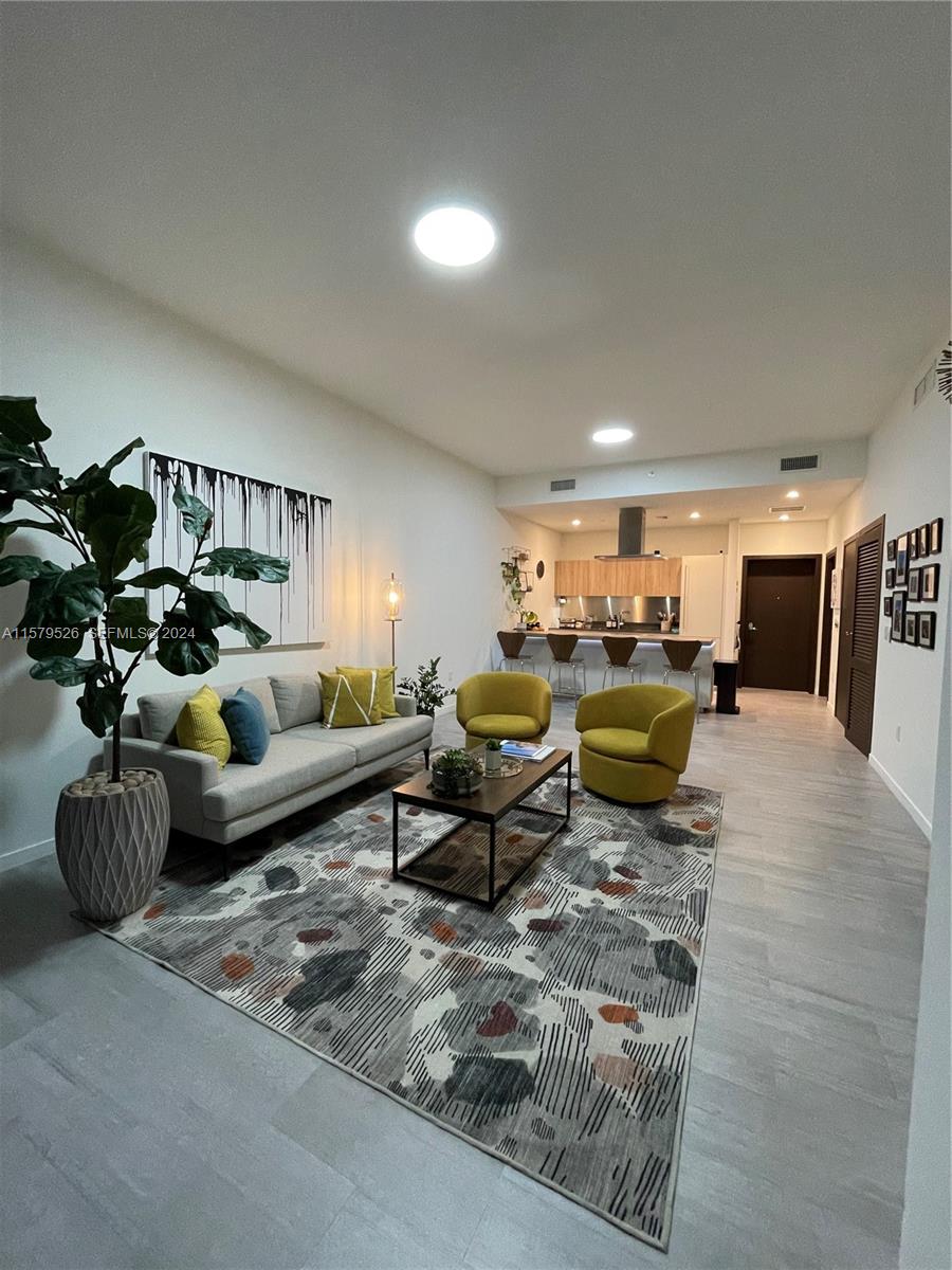 An open-concept living room features a grey sofa, yellow chairs, and a kitchen with bar seating — 1000 Brickell Plz # 1811, Miami FL 33131, MIAMI, FL