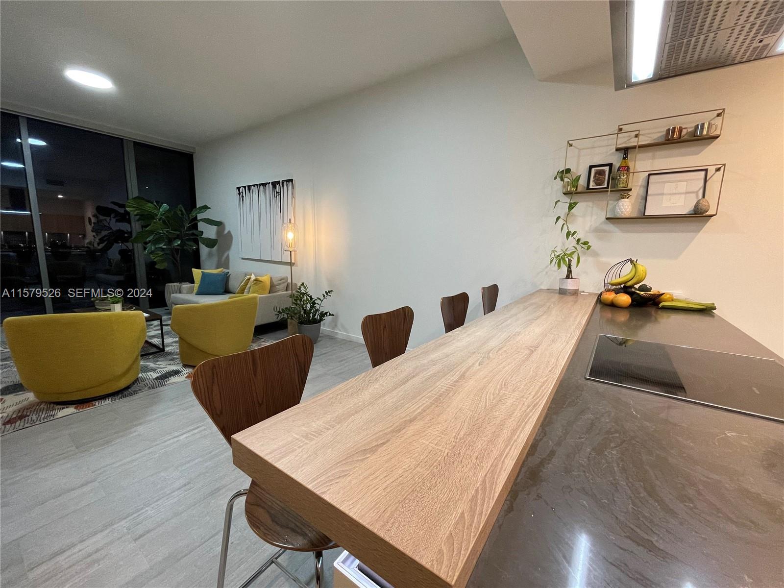 A modern kitchen island with a wood countertop faces a living area with yellow chairs — 1000 Brickell Plz # 1811, Miami FL 33131, MIAMI, FL
