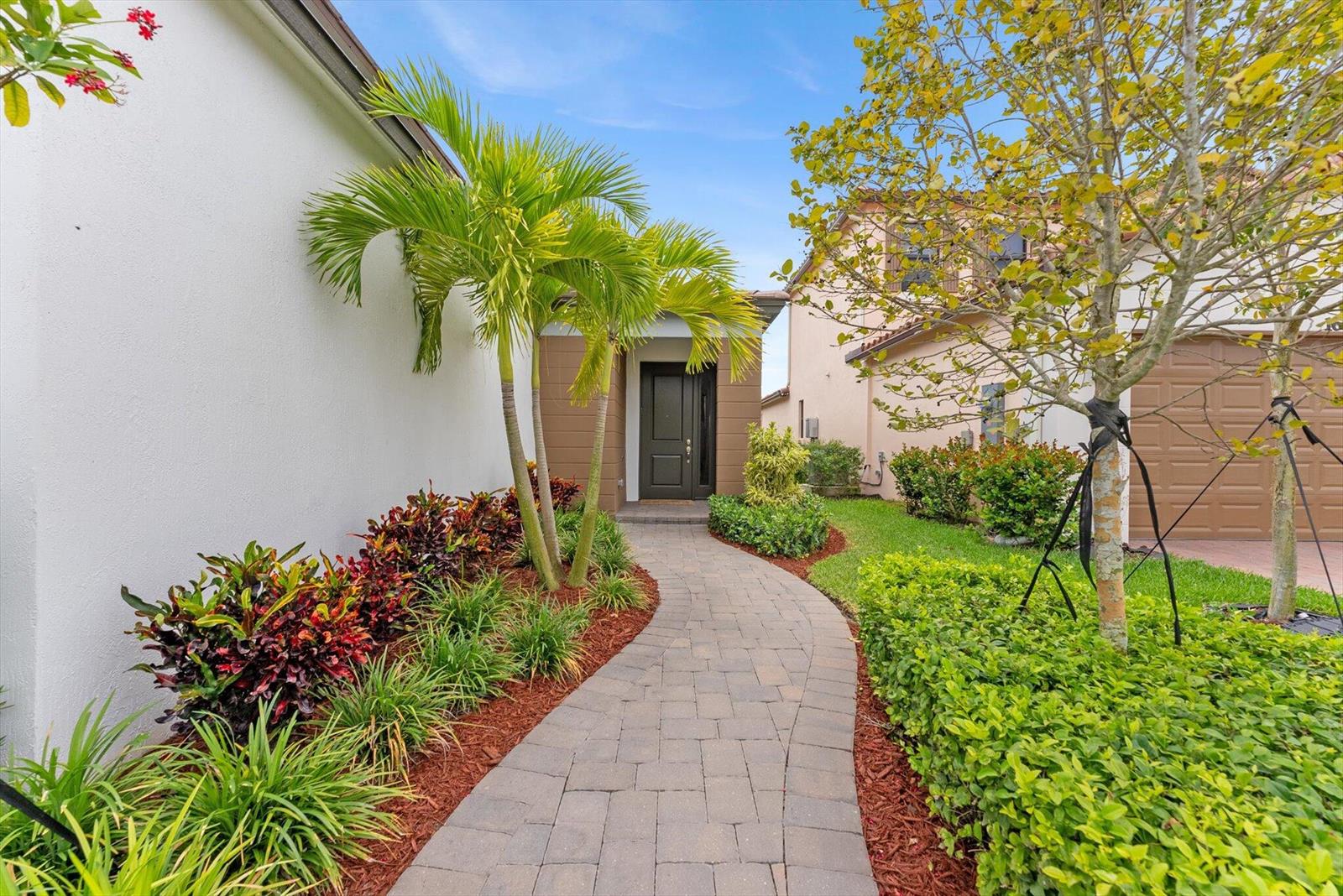 A paved walkway leads to the front entrance of a house with palm trees and landscaping — 16390 Sea Turtle Place, FL 33470, FL