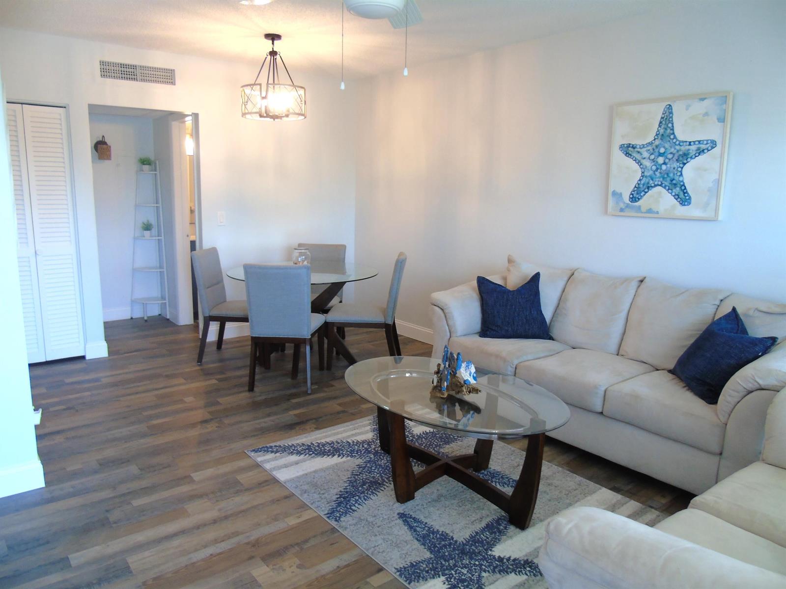 A living and dining area with wood-look flooring, a glass coffee table, and coastal decor — 309 Circle Drive S # 204, Boynton Beach FL 33435, BOYNTON BEACH, FL