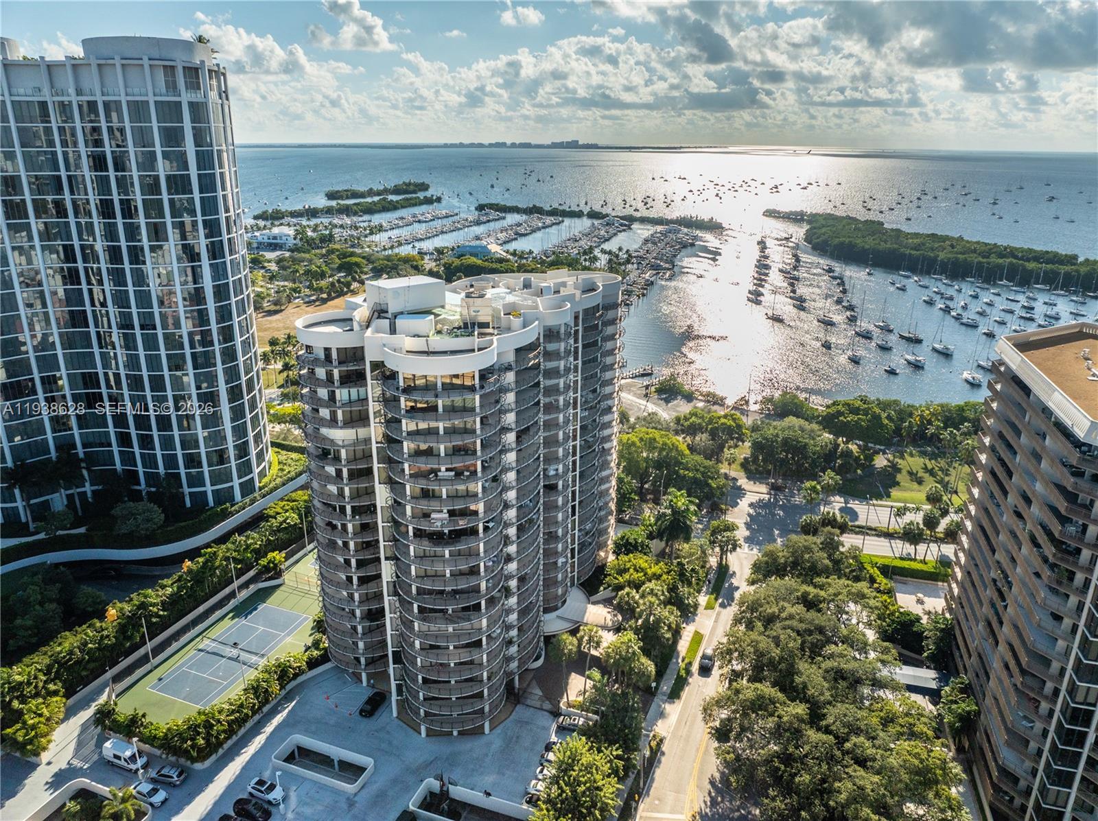 An aerial view shows high-rise residential buildings, a tennis court, and a marina with boats — 2843 S Bayshore Dr # 6B, Miami FL 33133, MIAMI, FL