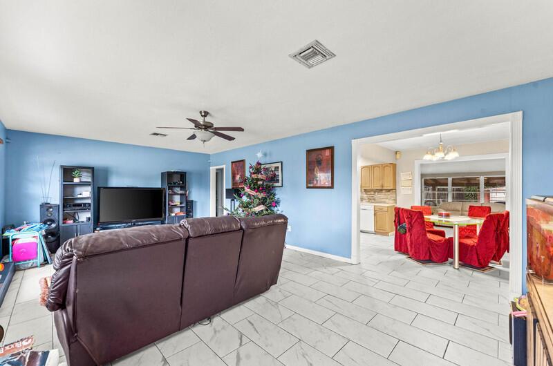 A living room with blue walls, tile flooring, and a dining area visible beyond — 305 Henthorne Drive, Palm Springs FL 33461, PALM SPRINGS, FL