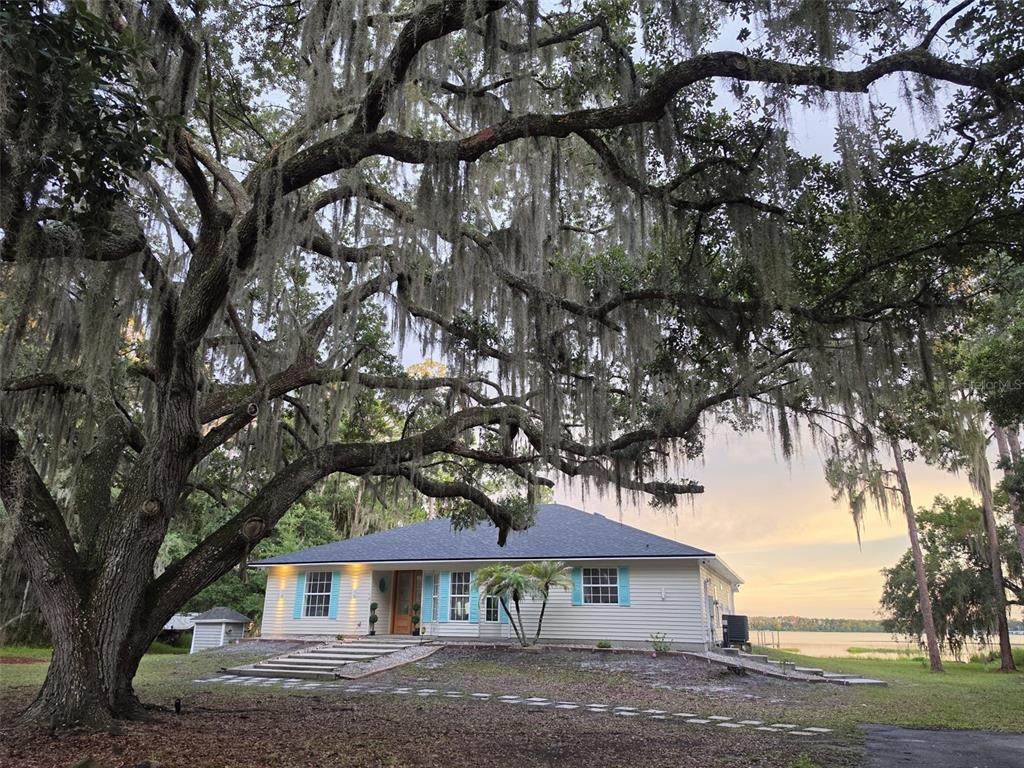 A single-story house with light siding and blue shutters sits under a large oak tree — 560 EDEN DRIVE, ST CLOUD, FL