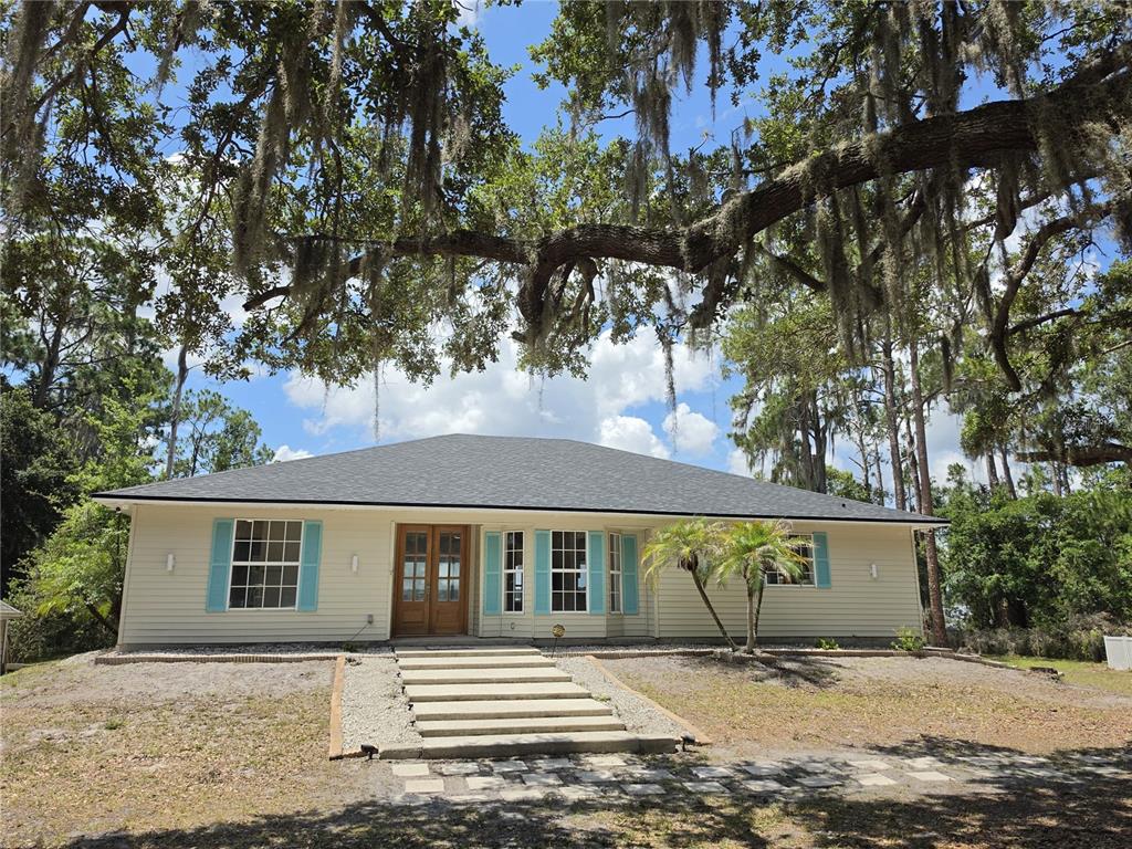 A single-story house with light siding, blue shutters, and a front staircase under large trees — 560 EDEN DRIVE, ST CLOUD, FL