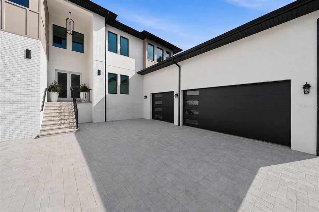 A modern two-story house exterior features a paved driveway, white brick walls, and black garage doors — 4706 W SAN CARLOS STREET, TAMPA, FL
