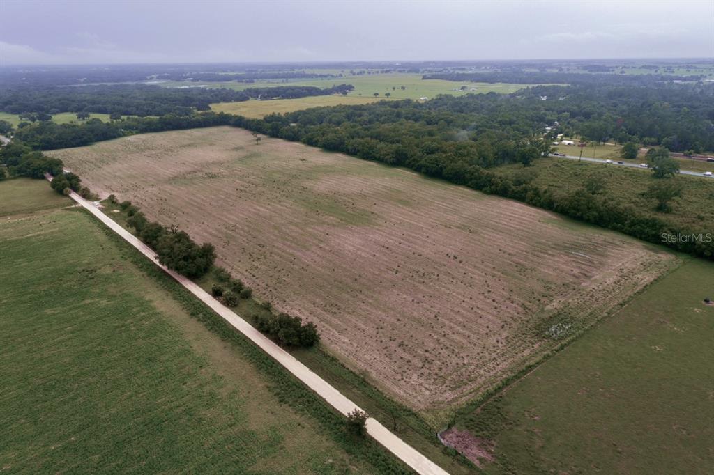 An aerial view shows a large, grassy field bordered by a dirt road and trees — 000 SE 200 AVENUE SE, MORRISTON, FL