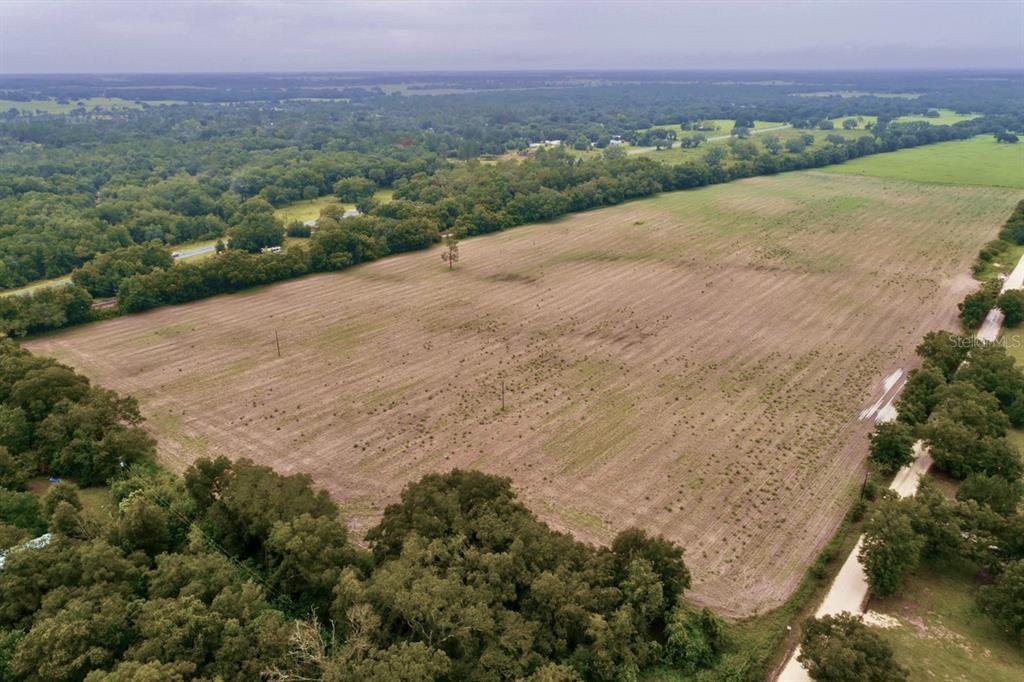 An aerial view shows a large, rectangular grassy field bordered by trees and a road — 000 SE 200 AVENUE SE, MORRISTON, FL