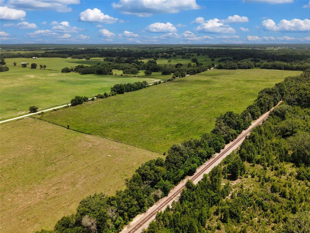An aerial view shows a large grassy pasture bordered by a railroad track and trees — 000 SE 200 AVENUE SE, MORRISTON, FL