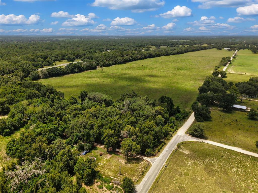 An aerial view shows a large, grassy field bordered by dense trees and a road — 000 SE 200 AVENUE SE, MORRISTON, FL