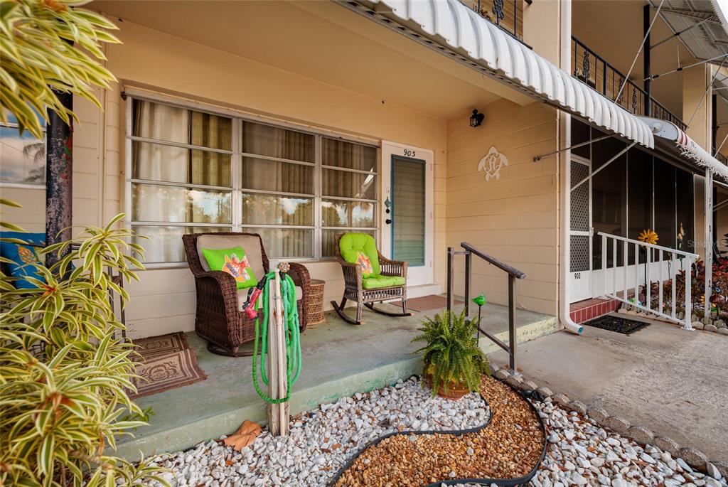 A patio with two wicker chairs, a green hose, and a small fern sits outside — 4143 56TH STREET N UNIT 903, KENNETH CITY, FL