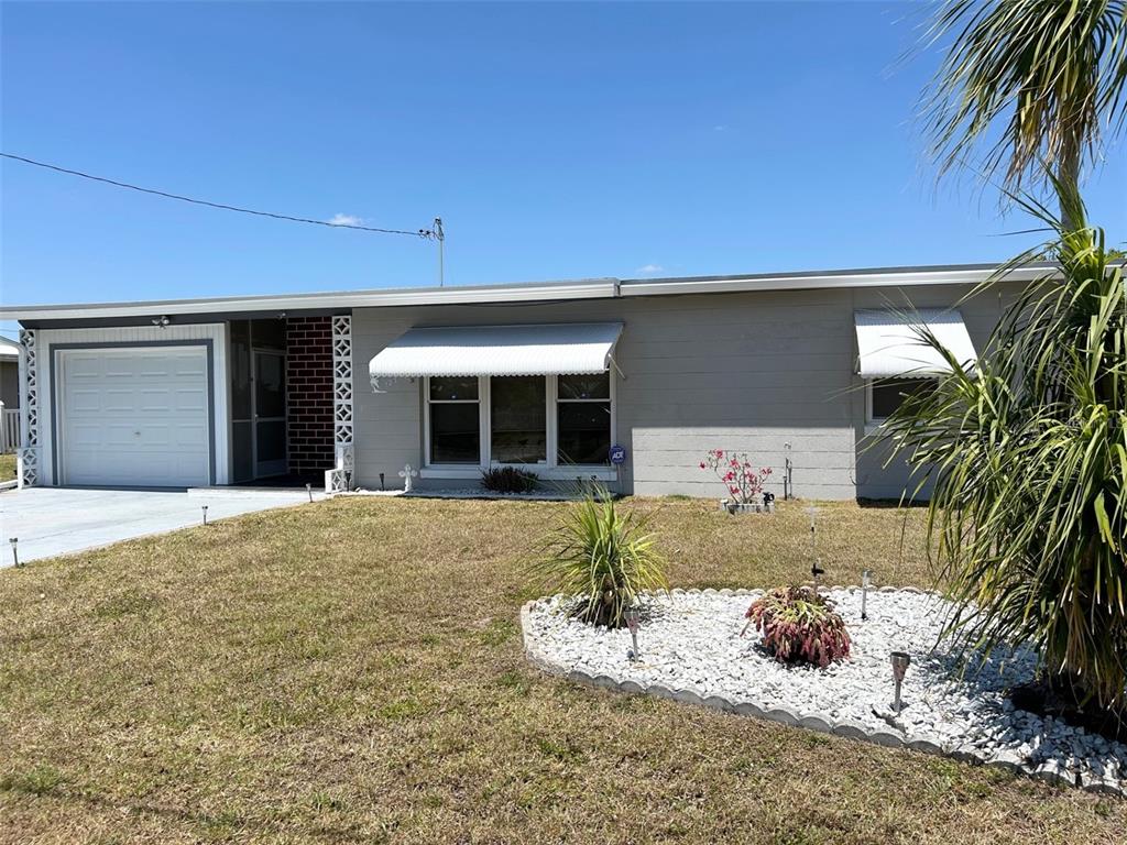 A single-story house with a gray exterior, a white garage door, and a rock garden — 123 POINSETTIA CIRCLE NE, PORT CHARLOTTE, FL