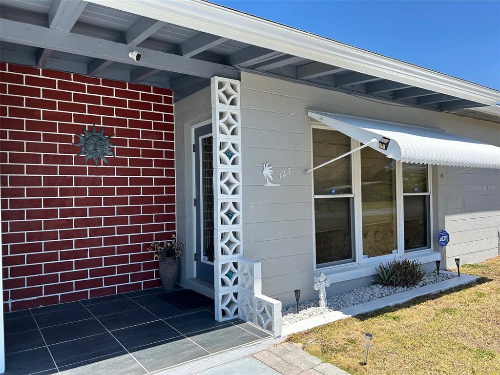 The exterior of a house features a red brick wall, a decorative breeze block column, and windows — 123 POINSETTIA CIRCLE NE, PORT CHARLOTTE, FL