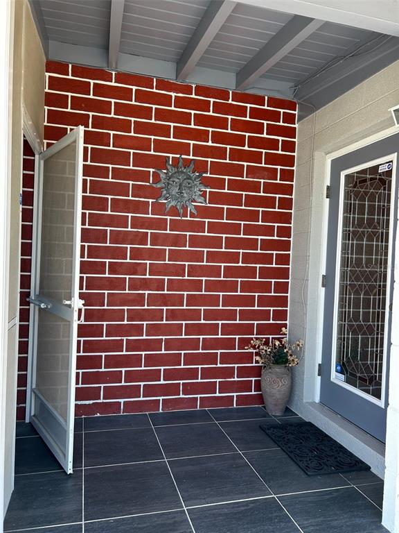 A covered entryway features a red brick wall, a sun ornament, and dark tiled flooring — 123 POINSETTIA CIRCLE NE, PORT CHARLOTTE, FL