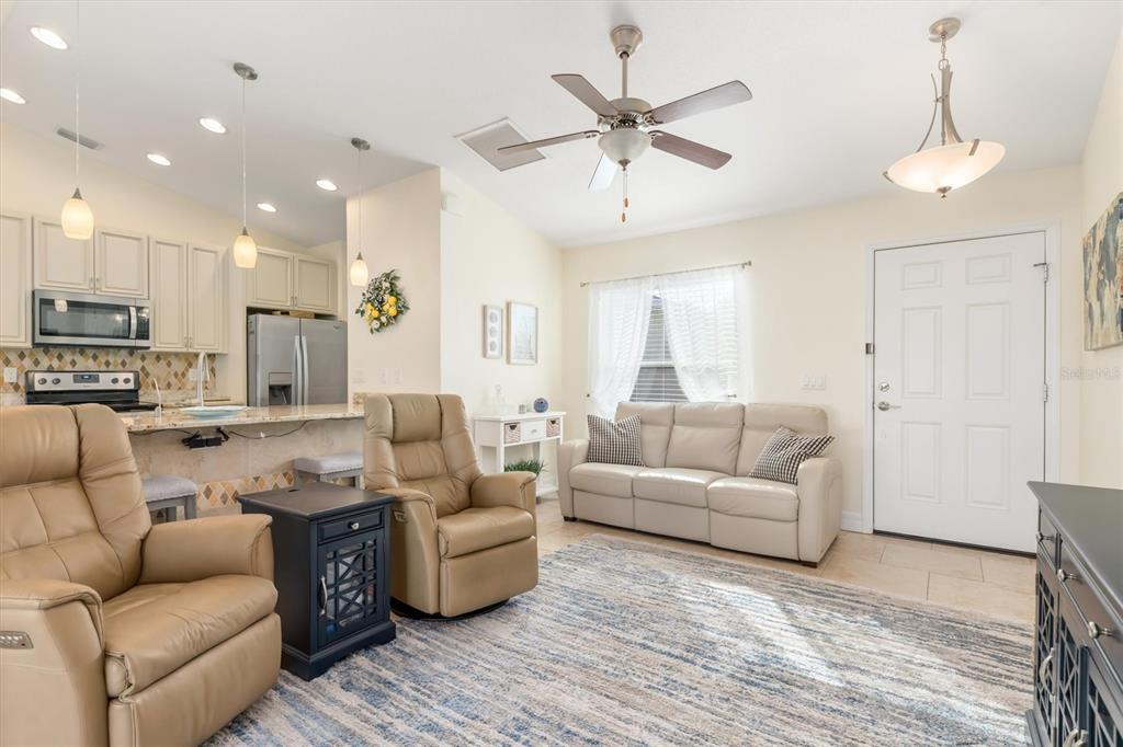 A living room with tan leather recliners and a sofa opens to a kitchen area — 4352 ADELAIDE AVENUE, NORTH PORT, FL