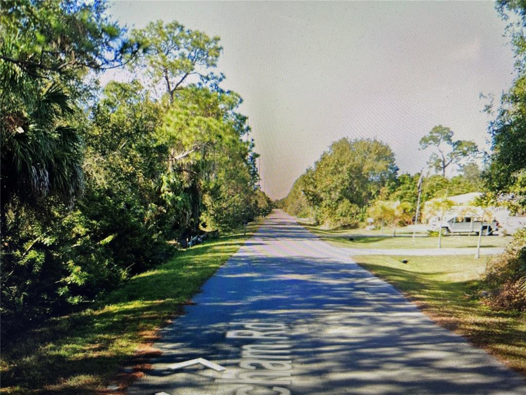 A paved road stretches into the distance, flanked by dense trees and a residential lawn — 26325 SCHAM ROAD, PUNTA GORDA, FL