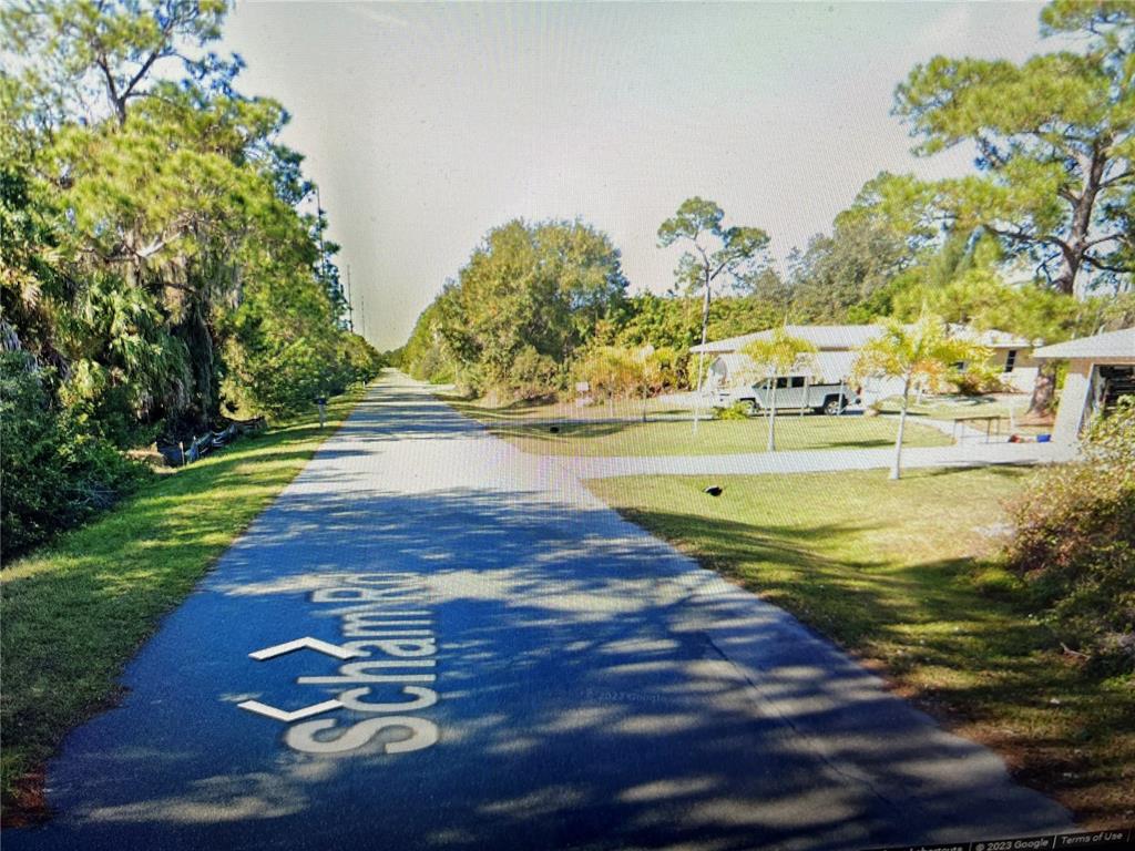 A paved road runs through a residential area with trees and a house on the right — 26325 SCHAM ROAD, PUNTA GORDA, FL