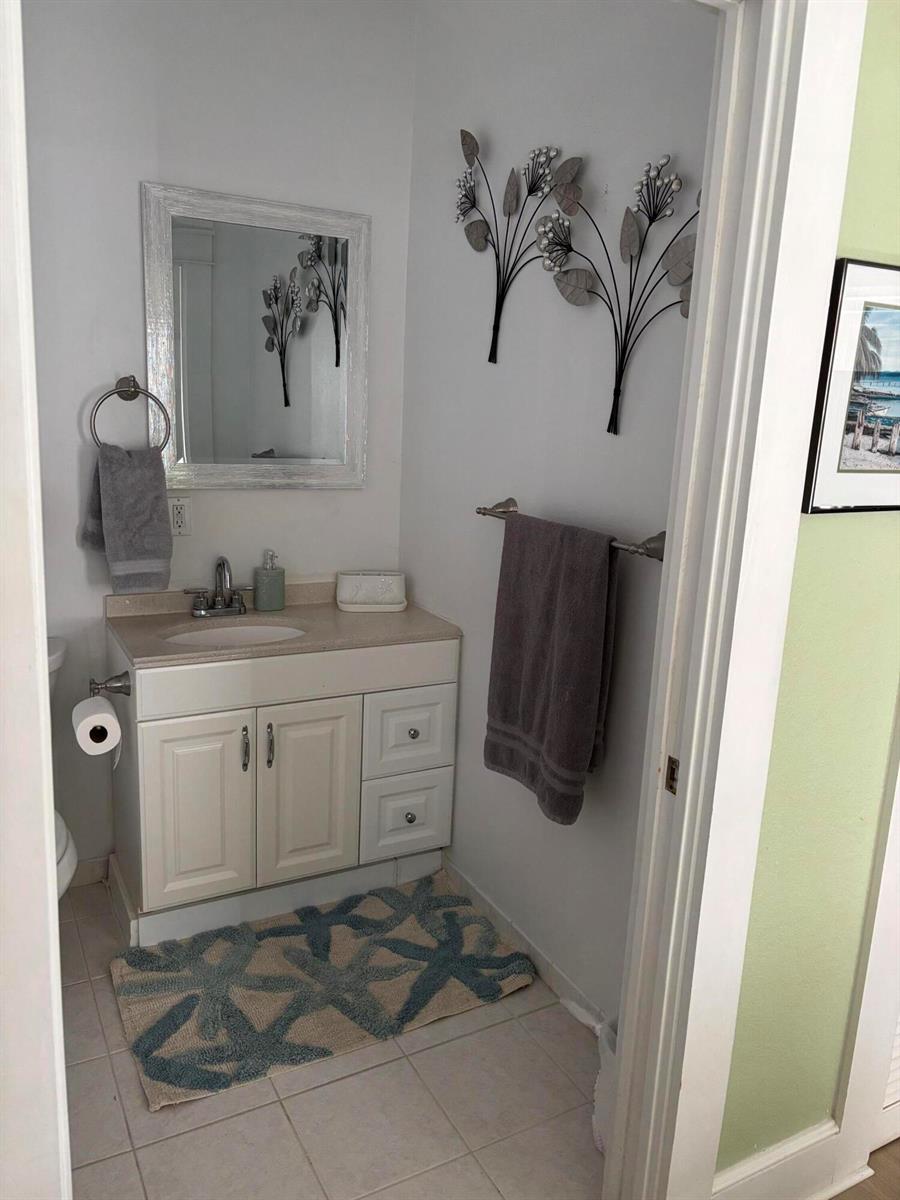 A small bathroom features a white vanity, a mirror, wall art, and a gray towel — 808 Kanuga Drive, West Palm Beach FL 33401, WEST PALM BEACH, FL