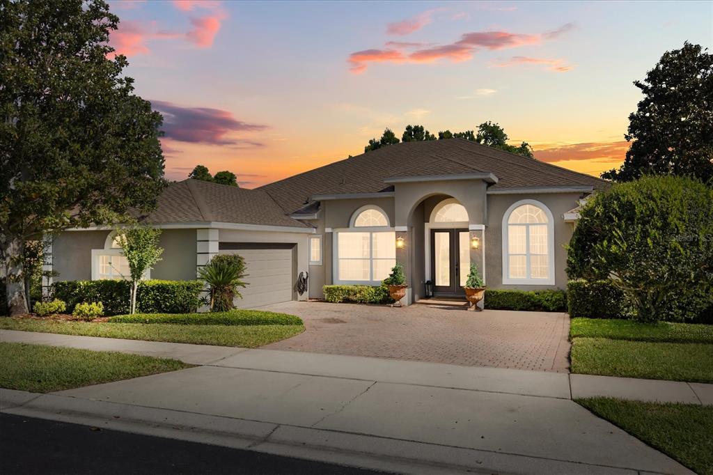 A single-story house with a paved driveway, arched windows, and a garage at sunset — 2210 NORTHUMBRIA DRIVE, SANFORD, FL