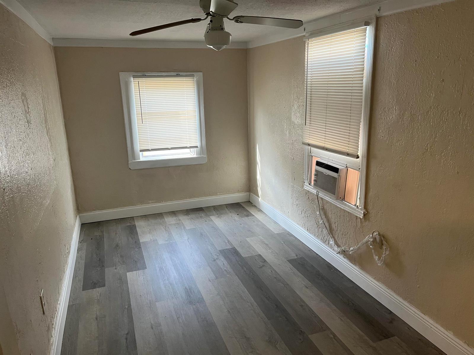 A small bedroom with beige walls, grey wood-look flooring, a ceiling fan, and window unit — 611 N Broadway # A, Lantana FL 33462, LANTANA, FL