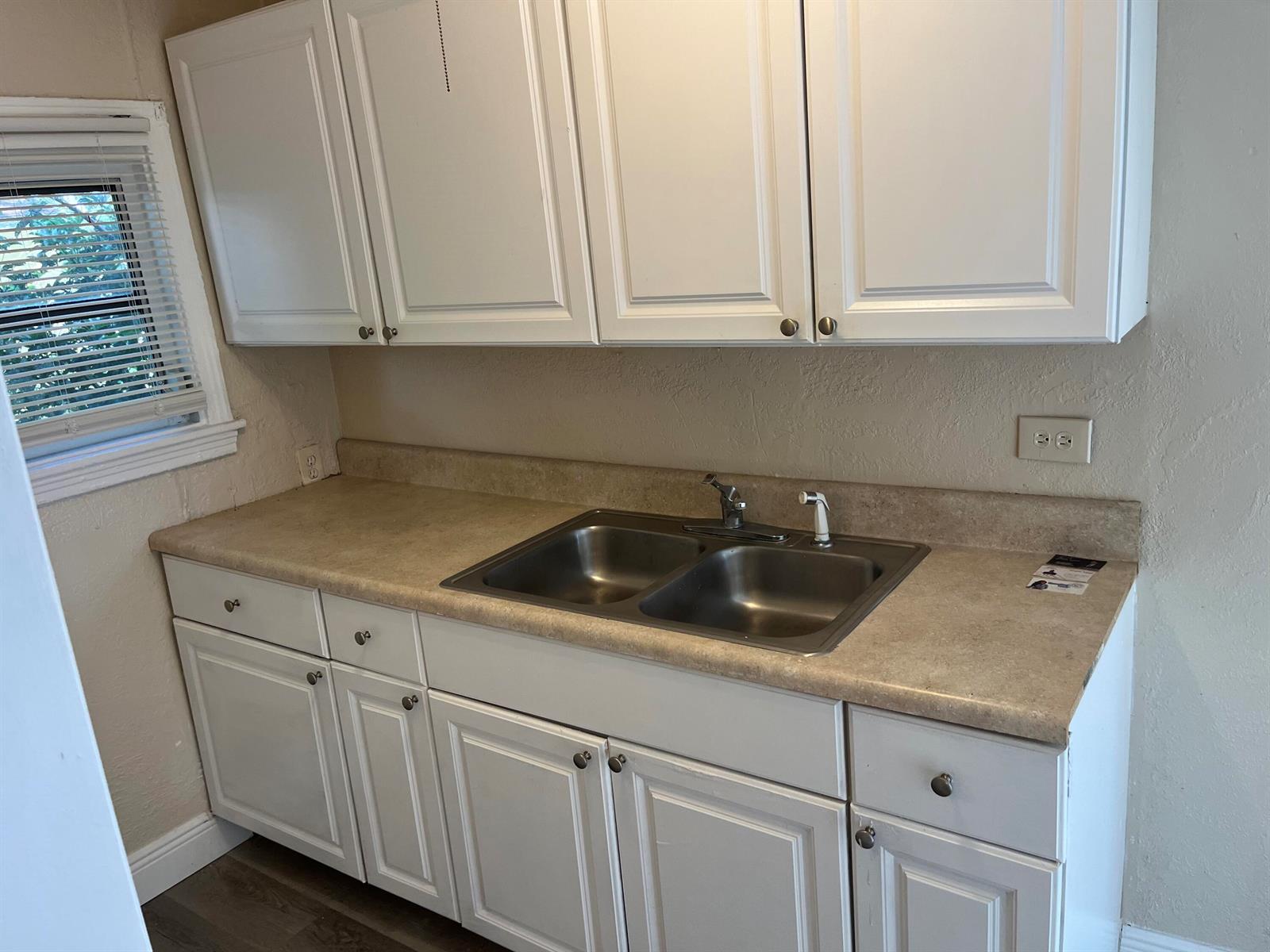 A kitchen features white cabinets, a beige laminate countertop, and a double-basin stainless steel sink — 611 N Broadway # A, Lantana FL 33462, LANTANA, FL