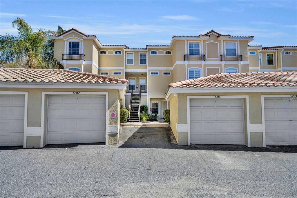 A multi-story apartment building features tan stucco walls, tile roofs, and several garage doors — 676 SANDY NECK LANE UNIT 102, ALTAMONTE SPRINGS, FL