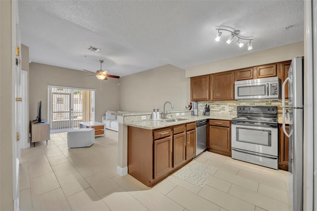 An open-concept kitchen with wood cabinets and granite countertops overlooks a living area with tile — 676 SANDY NECK LANE UNIT 102, ALTAMONTE SPRINGS, FL