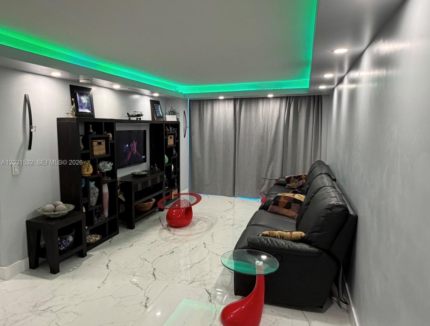 A living room features a black entertainment unit, a leather sofa, and green ceiling lighting — 3140 S Ocean Dr # 1003, Hallandale Beach FL 33009, HALLANDALE BEACH, FL