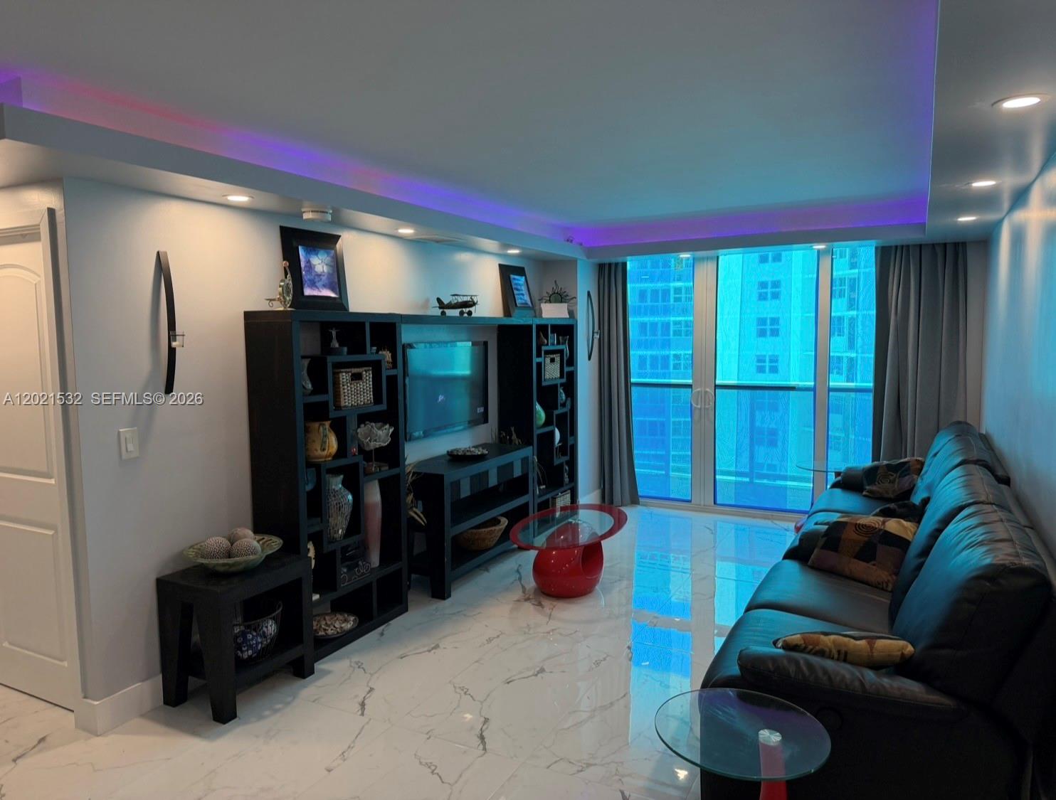 A living room features black shelving, a leather sofa, marble floors, and purple ceiling lighting — 3140 S Ocean Dr # 1003, Hallandale Beach FL 33009, HALLANDALE BEACH, FL