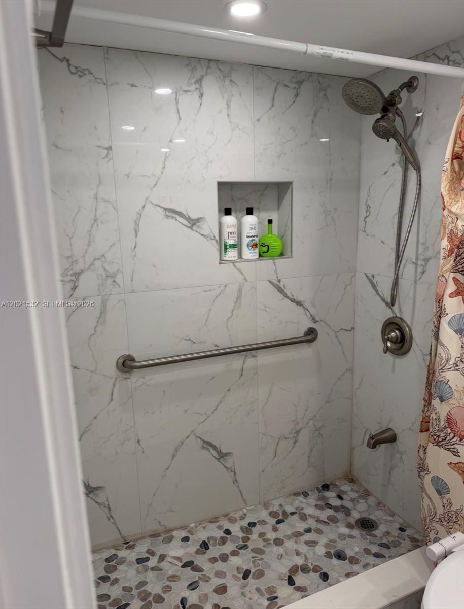A shower features marble-look wall tiles, a pebble floor, a grab bar, and a handheld sprayer — 3140 S Ocean Dr # 1003, Hallandale Beach FL 33009, HALLANDALE BEACH, FL