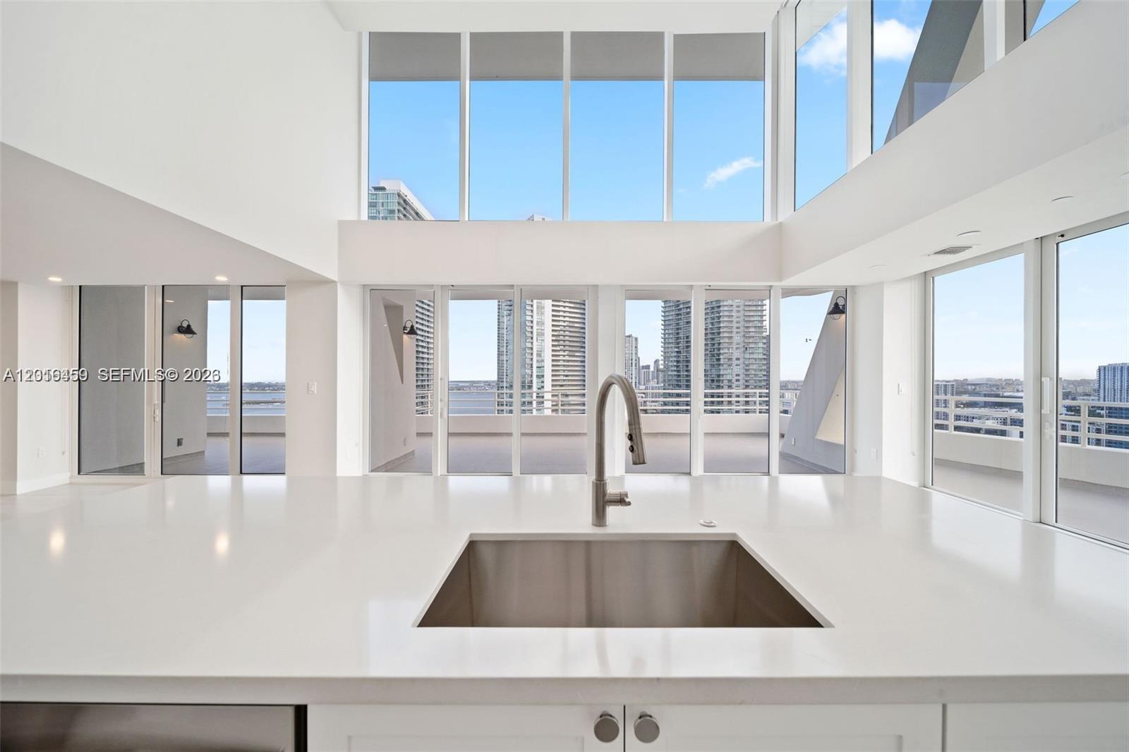 A modern kitchen island with a stainless steel sink overlooks a balcony and city skyline — 555 NE 34th St, Miami FL 33137, MIAMI, FL