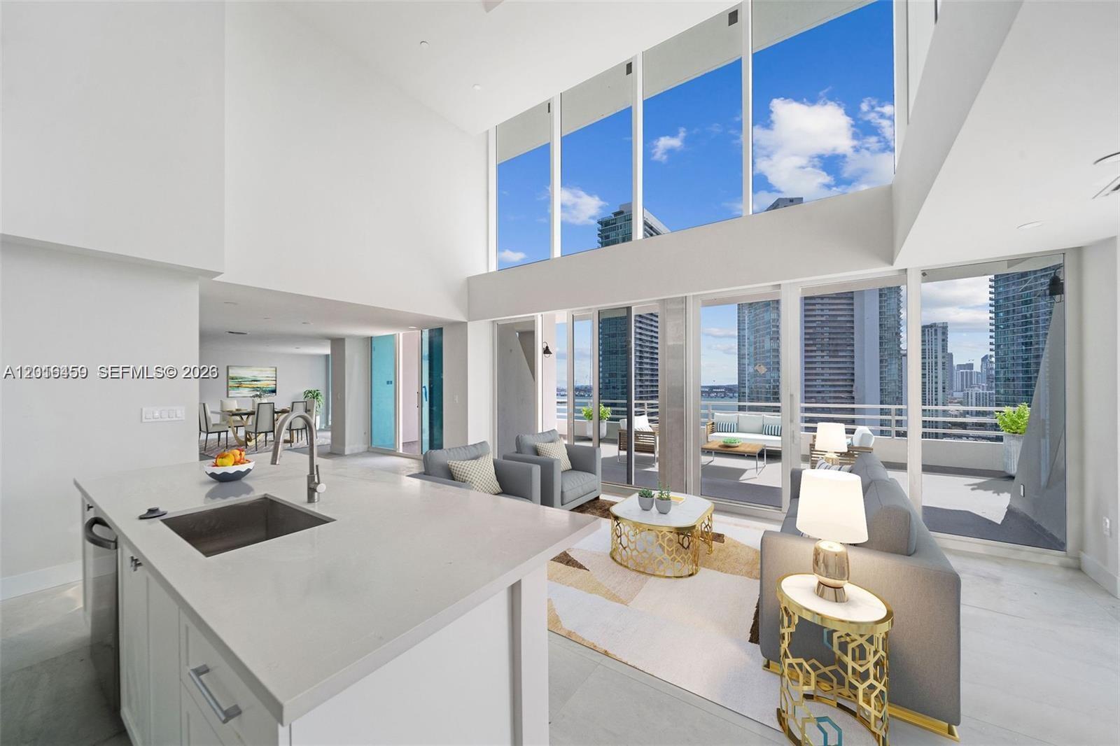 A modern kitchen overlooks a double-height living room with floor-to-ceiling windows and a balcony — 555 NE 34th St, Miami FL 33137, MIAMI, FL