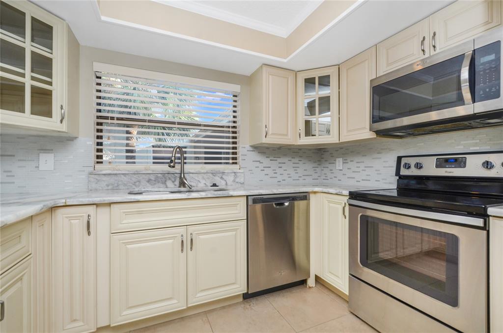 A kitchen features cream-colored cabinets, stainless steel appliances, a marble countertop, and a tiled backsplash — 439 S NETHERWOOD CRESCENT UNIT 439, ALTAMONTE SPRINGS, FL